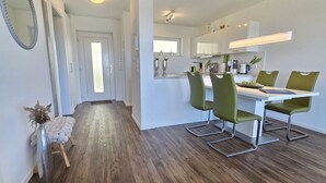 A modern kitchen with white cabinets, green chairs, and a wooden floor. - 47.3.M Seestern - Well-kept apartment with sea view, infrared cabin, large balcony (Wangerland)