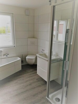 Une salle de bain moderne équipée d’une baignoire, de toilettes et d’une douche à parois de verre.