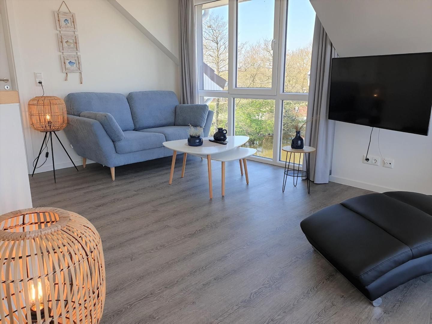 Ein modernes Wohnzimmer mit grauem Sofa, einem weißen Couchtisch, einer schwarzen Ledercouch und einem großen Fernseher.