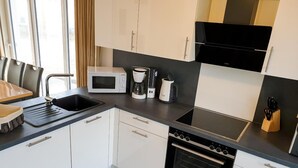 A modern kitchen with white cabinets, a black countertop, a microwave, a coffee maker, a toaster, and an oven. - House no. 07, Ferienhaus Deichgraf - Modern vacation home, sauna, south-facing terrace, (Wangerland)