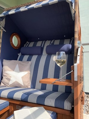 Un coin salon confortable, avec des coussins rayés, un oreiller en forme d’étoile, un miroir rond et un verre de vin posé sur une table en bois.