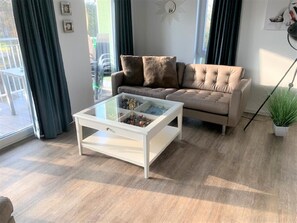 A living room with a beige sofa, a glass coffee table, and a potted plant. - 47.1.S Waterkant - Cozy, well-kept vacation apartment near the beach, own (Wangerland)