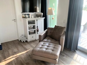 Ett modernt vardagsrum med en beige soffa, ett vitt skåp med förvaringsutrymme, en tv och ett fönster med gardiner.