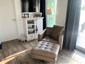 Un salon moderne avec un canapé beige, un meuble blanc avec des rangements, un téléviseur et une fenêtre avec des rideaux.