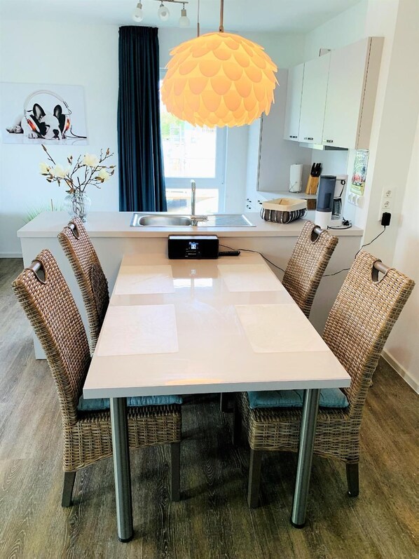 A modern dining area with a white table, wicker chairs, and a unique orange pendant light. - 47.1.S Waterkant - Cozy, well-kept vacation apartment near the beach, own (Wangerland)
