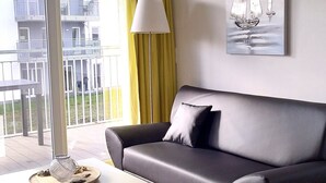 En moderne stue med en grå sofa, et lille bord med en dekorativ genstand, en gulvlampe og et maleri af sejlbåde på væggen.