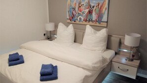 Et hotelværelse med en seng, to sengeborde med lamper, et billede på væggen og trægulv.