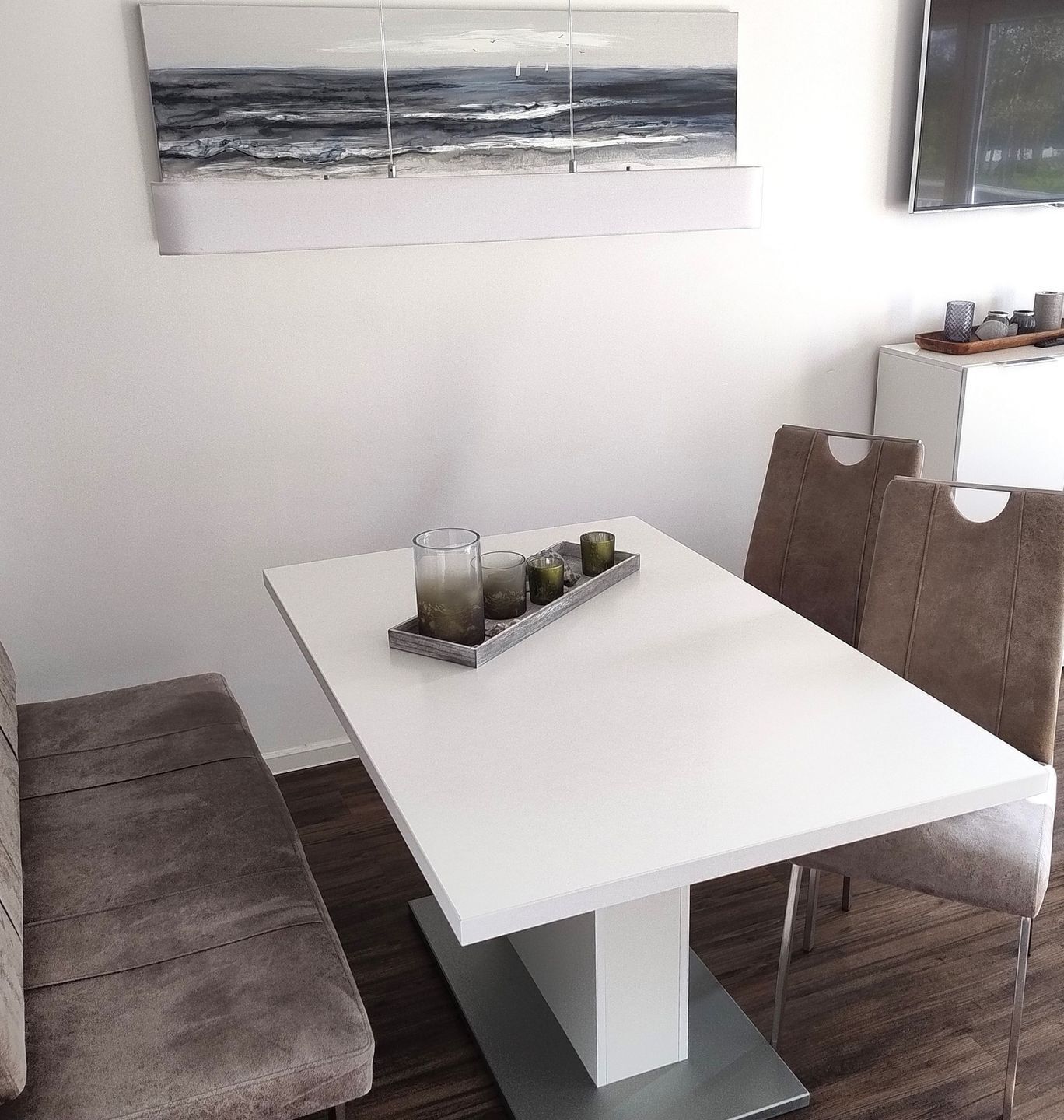 Un comedor moderno con una mesa blanca, sillas acolchadas y un candelabro de vidrio con velas.
