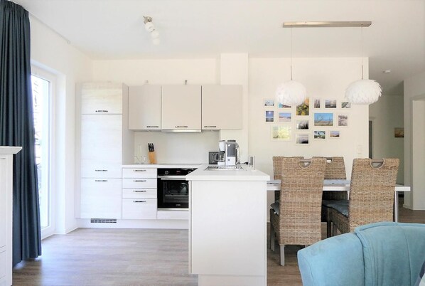 Una cucina moderna con mobili bianchi, forno integrato e zona pranzo con sedie in vimini e un divano blu.