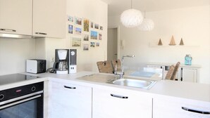 A modern kitchen with white cabinetry, a built-in oven, a coffee maker, and a sink. - 47.0.S Waterkant - Ground floor apartment with direct Graft location, sauna, beach nearby (Wangerland)