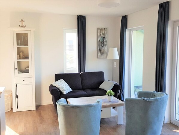 Un salon moderne avec un canapé foncé, deux fauteuils, une table basse et un meuble avec des portes en verre.