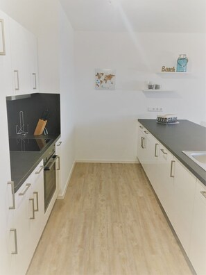 Una cocina moderna con armarios blancos, encimera negra y suelo de madera.