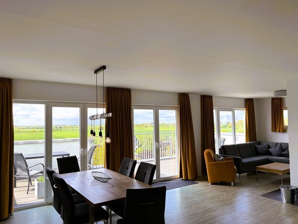 A spacious living area with a dining table, sofa, and a balcony with a view of a green landscape. - 47.6.S Dwarslöper - Family-friendly apartment with far-reaching views, 2 bathrooms, (Wangerland)