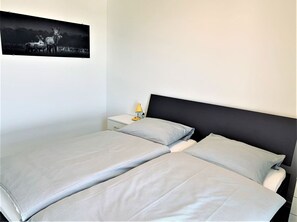 Una cama doble con cabecera negra, una mesita de noche con lámpara y un cuadro enmarcado en la pared.