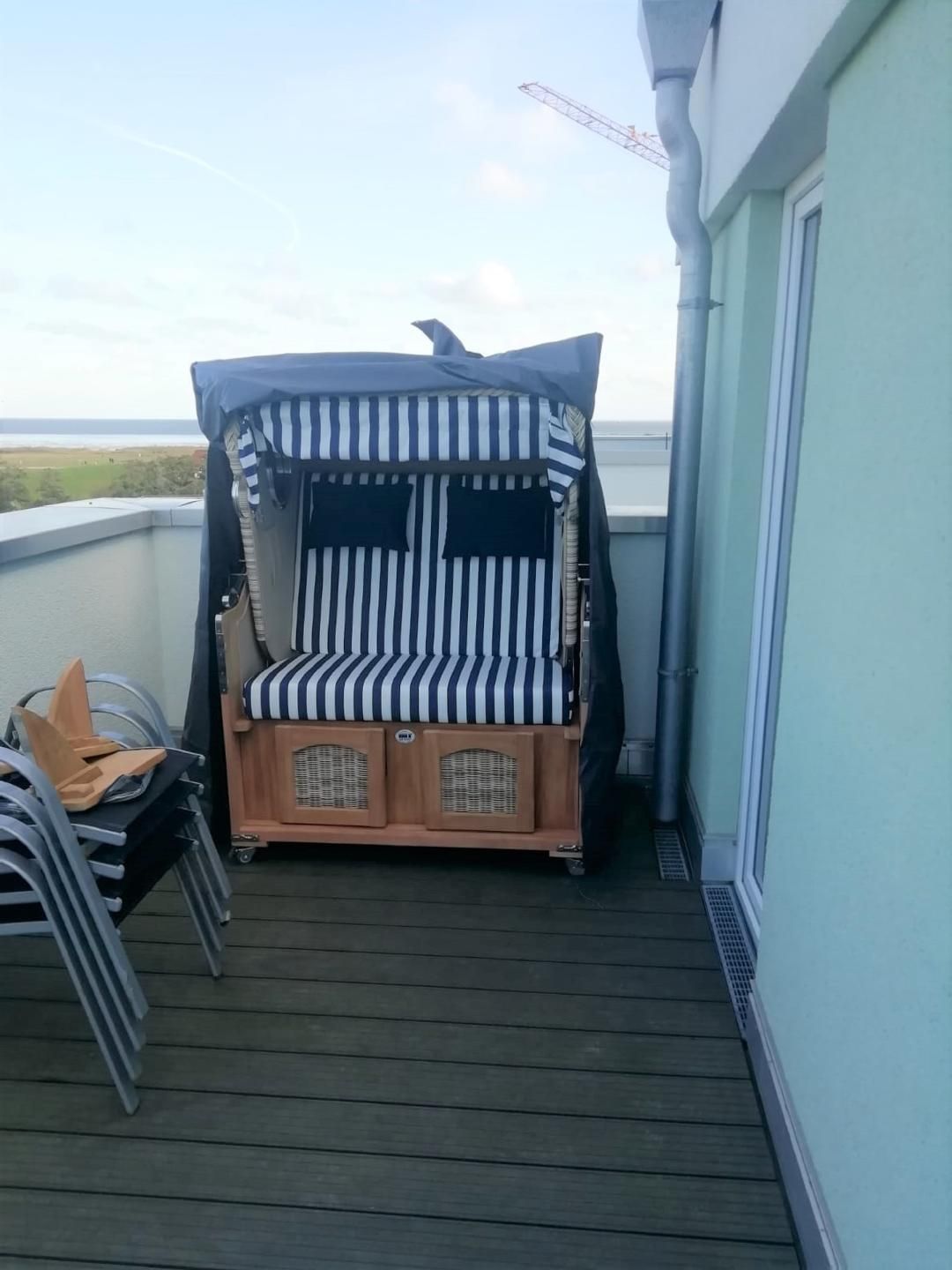Ein überdachter Sitzbereich im Freien mit gestreiften Kissen und einem Baldachin, neben einem Gebäude mit weißer Fassade und Blick auf das Meer.