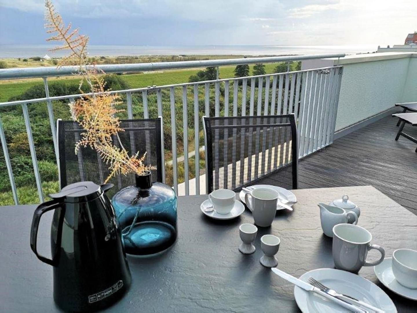 A table set for tea on a balcony with a view of the sea and greenery.