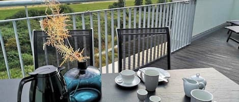 Una mesa dispuesta para el té en un balcón con vista al mar y al verdor.