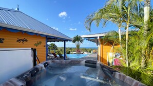 A hot tub with a view of the ocean, a pool, and a covered patio area with lounge chairs.