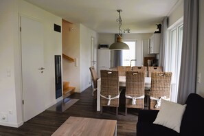 Ein modernes Wohnzimmer mit Essbereich, ausgestattet mit Korbstühlen, einem Holztisch und einem schwarzen Sofa.