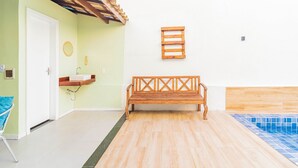 A room with a wooden bench, a white door, a small wooden shelf with a sink, and a tiled pool area. - GB45 Excelente Casa 4 Suítes - Guarajuba (Camaçari)
