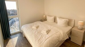 Un dormitorio con una cama grande, dos mesitas de noche, un ventanal con cortinas y vistas a la ciudad.
