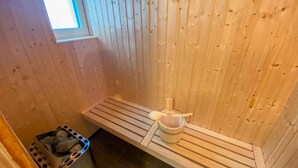 Una sala de sauna con paredes de madera, un banco, un cubo y un bote de basura.