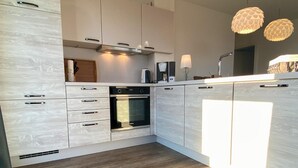 Una cocina moderna con armarios blancos, horno empotrado y suelo de madera.