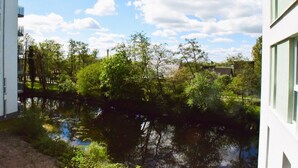 Blick auf einen Fluss mit Bäumen und Gebäuden im Hintergrund.