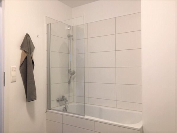 Un baño moderno con ducha acristalada, bañera blanca y toalla colgada en la pared.