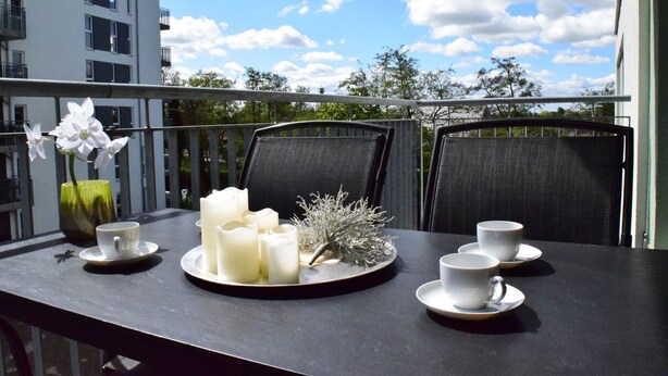 Ein Balkon mit Tisch für zwei Personen, ausgestattet mit weißen Kerzen, einer Vase mit weißen Blumen und zwei Tassen.