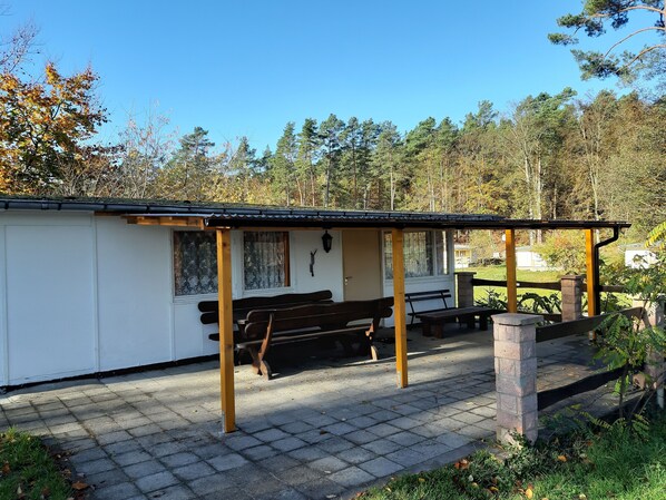 A small, single-story building with a covered patio area, a bench, and a stone pillar.