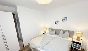 A bedroom with a bed, nightstands, a wardrobe, and two wall-mounted pictures.
