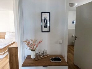 Een slaapkamer met een bed, een nachtkastje met een telefoon, een vaas met gedroogde bloemen en een lijst met een afbeelding aan de muur.