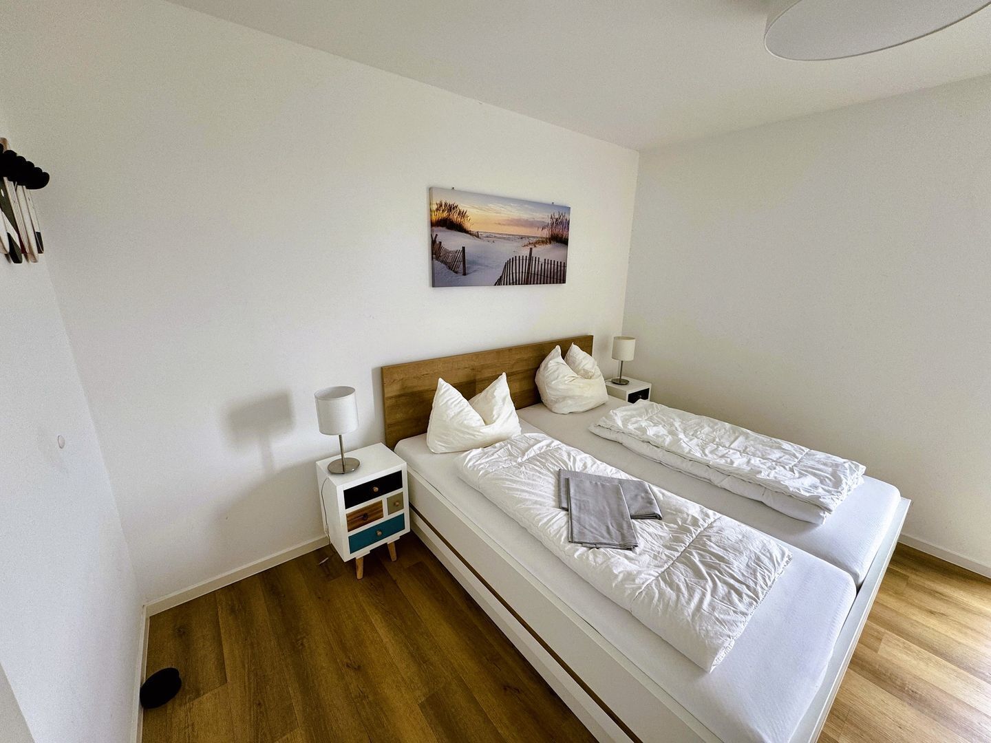 A hotel room with two beds, a nightstand with a lamp, a small drawer unit, and a painting on the wall.