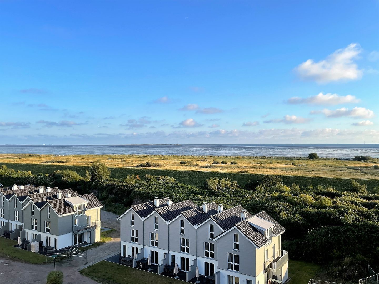 A residential area with modern houses, a grassy field, and a view of the sea.