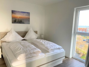 Ein modernes Schlafzimmer mit Bett, Kissen, Nachttisch, Lampe und einem Bild an der Wand.