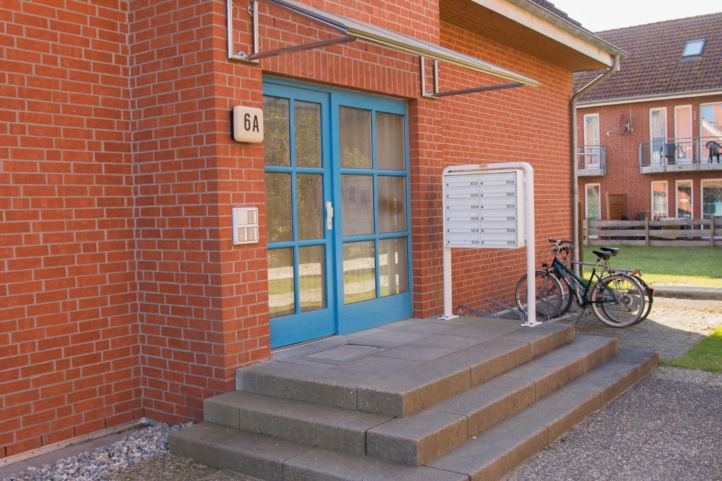 Un bâtiment en briques rouges avec une porte bleue, portant le numéro 6A, et un vélo garé à l’extérieur.