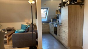 A modern kitchen with wooden cabinets, a built-in oven, and a dining area with a sofa and a coffee table. - Domicil - Evening sun - "Domicil" Enjoy the evening sun! (Dahme)
