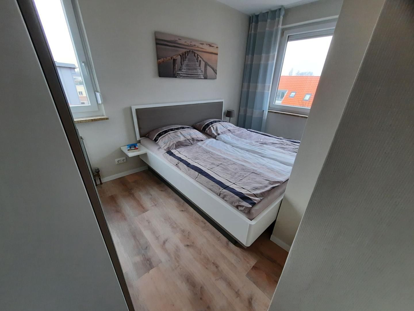 A bedroom with a bed, a nightstand, a wall-mounted painting, and a window with curtains.