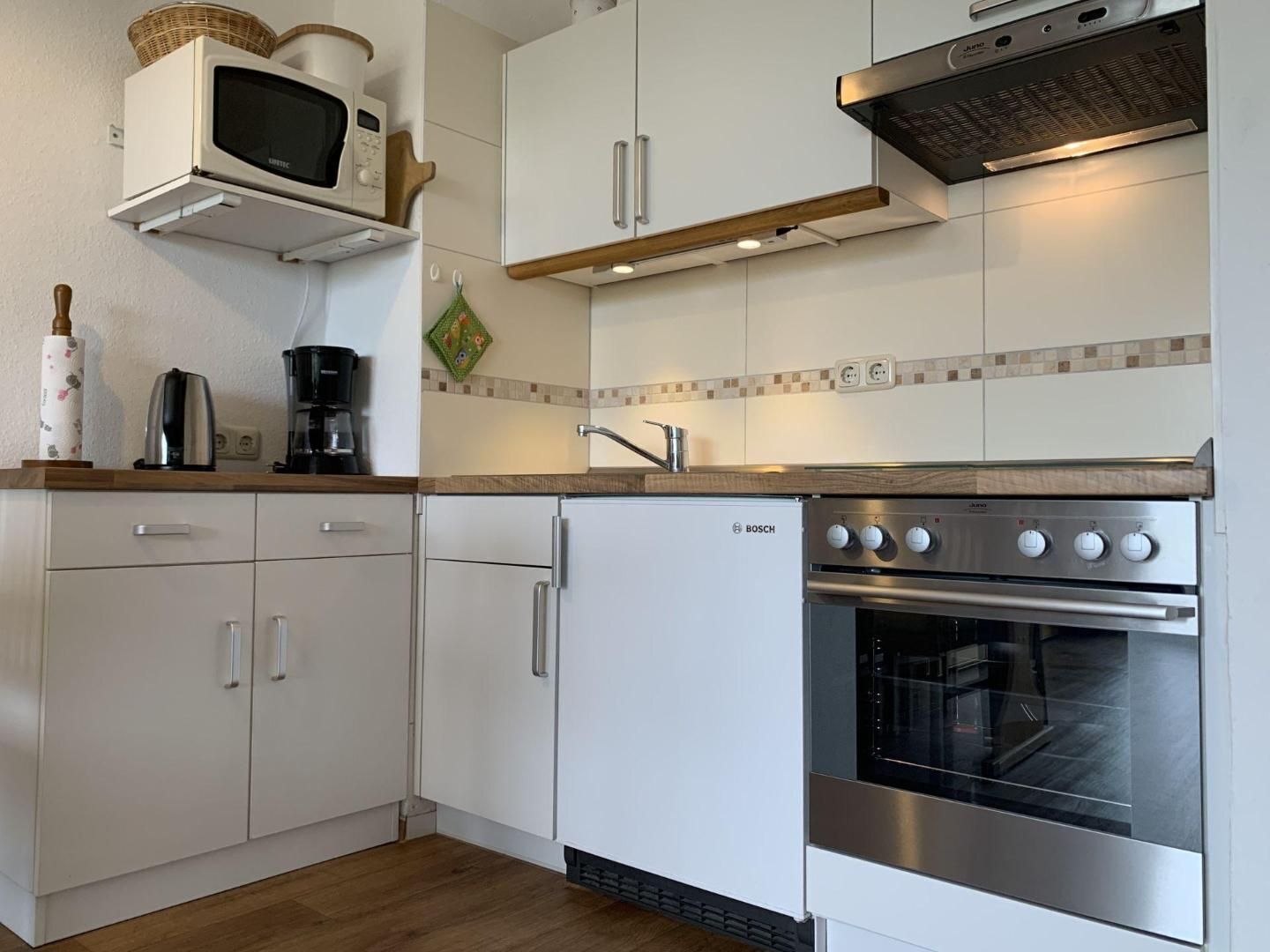 A kitchen with white cabinets, a Bosch refrigerator, a microwave, a coffee maker, and a stainless steel oven.