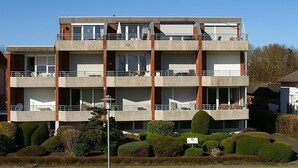 Un edificio de varios pisos con balcones, una señal que indica una ubicación específica y jardines bien cuidados.