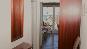 Un pasillo con un banco de madera, una puerta que da a un balcón con vistas al mar y un comedor con mesa y sillas.