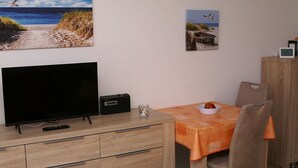 Una habitación con televisión, radio, una mesa con un tazón y una silla.