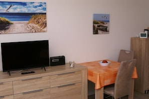 A room with a TV, a radio, a table with a bowl, and a chair.