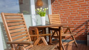 A wooden deck with outdoor furniture including chairs and a table, a potted plant, and a brick wall in the background. - Welcome to Dahme! - House on the dike (Dahme)