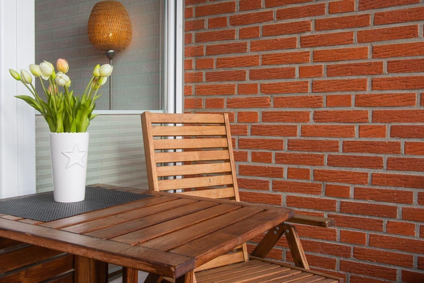 A wooden table and chairs set against a brick wall, with a white vase with tulips on the table.