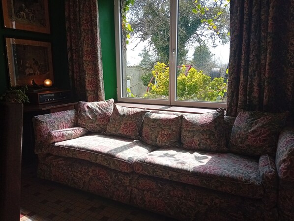 Una habitación acogedora con un sofá estampado con motivos florales, una pared verde y una ventana con cortinas.
