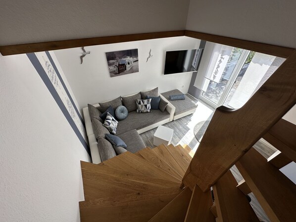 A modern living room with a grey sofa, a flat-screen TV, and a wooden staircase.