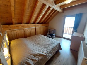 A cozy room with a wooden ceiling, a bed with a quilt, a small table, and a window with curtains.