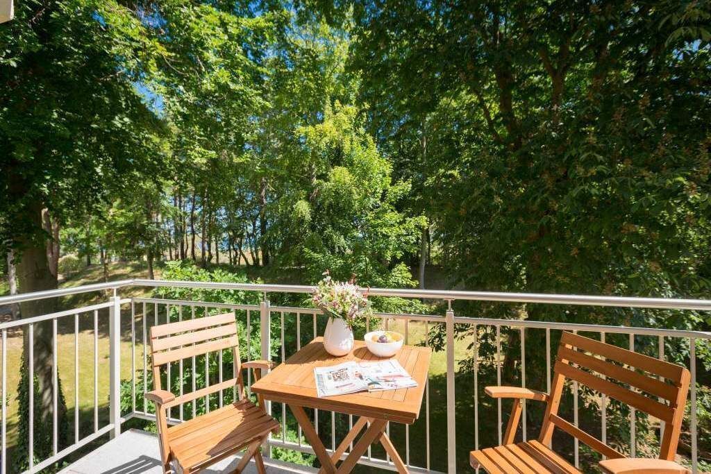 Een balkon met houten meubels, een tafel met een vaas en schaal, en een krant.
